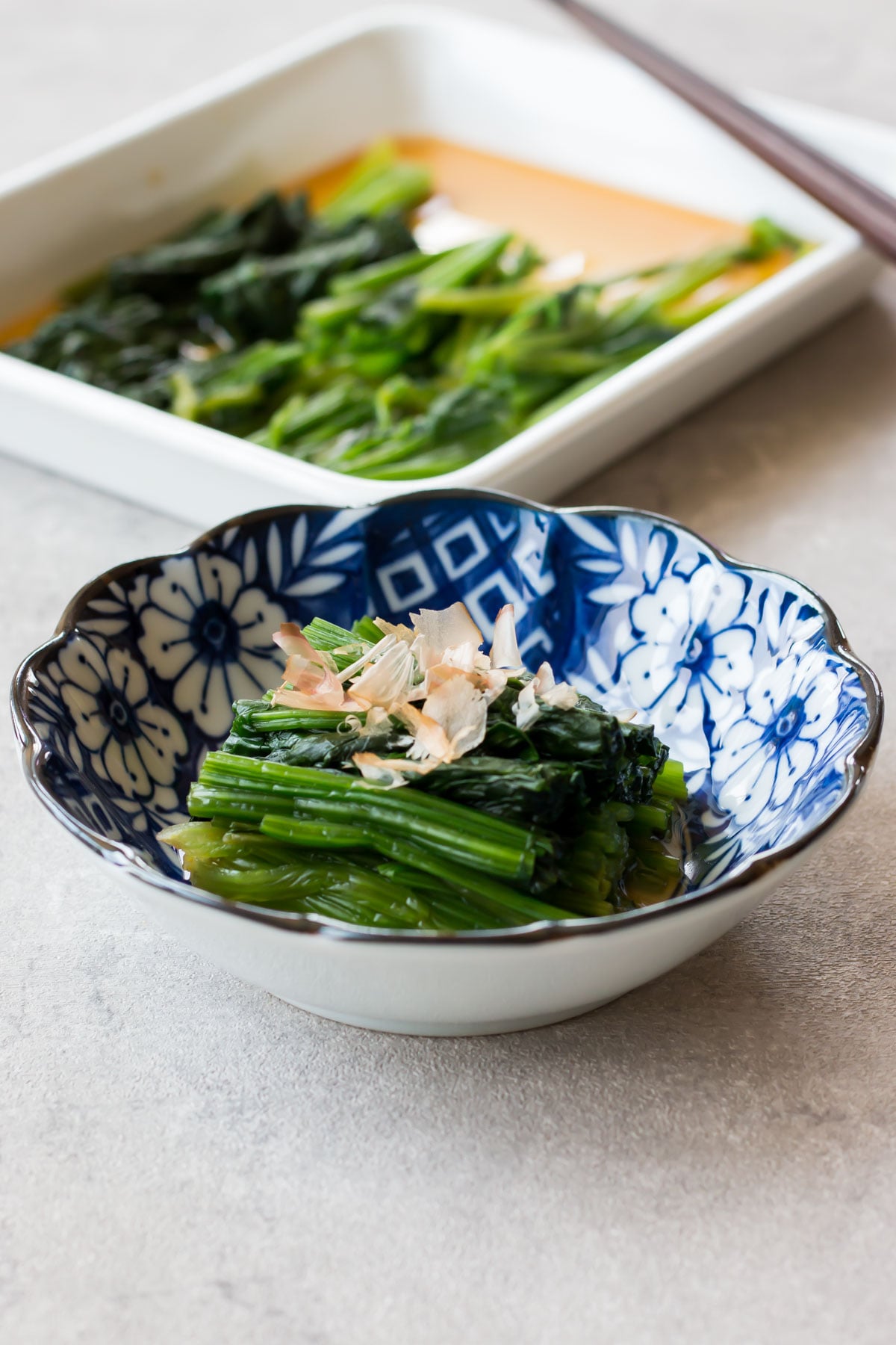 Spinach ohitashi served on a small plate with bonito flakes.