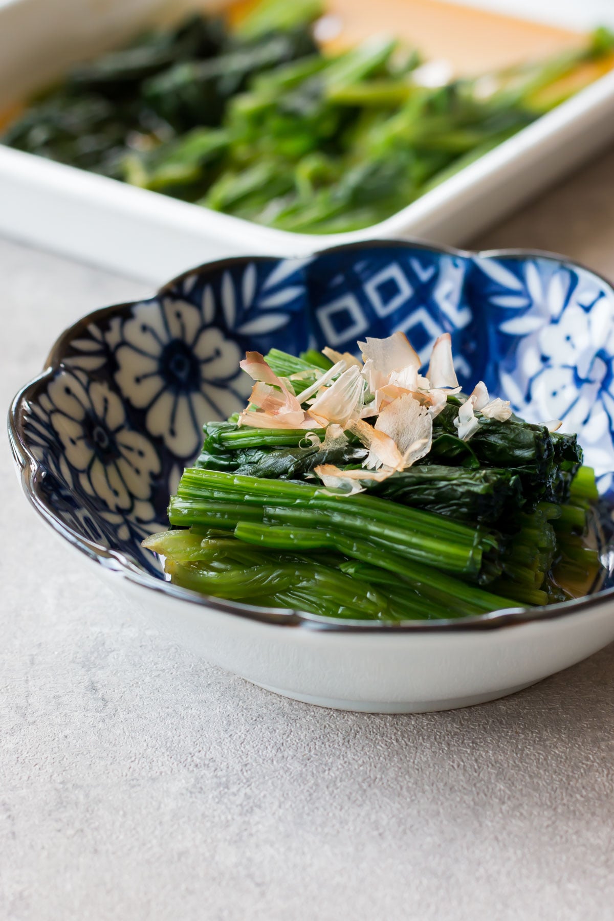 Spinach ohitashi served on a small plate with bonito flakes.