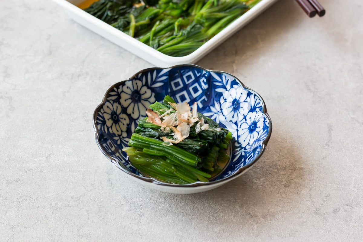 Spinach ohitashi served on a small plate with bonito flakes.