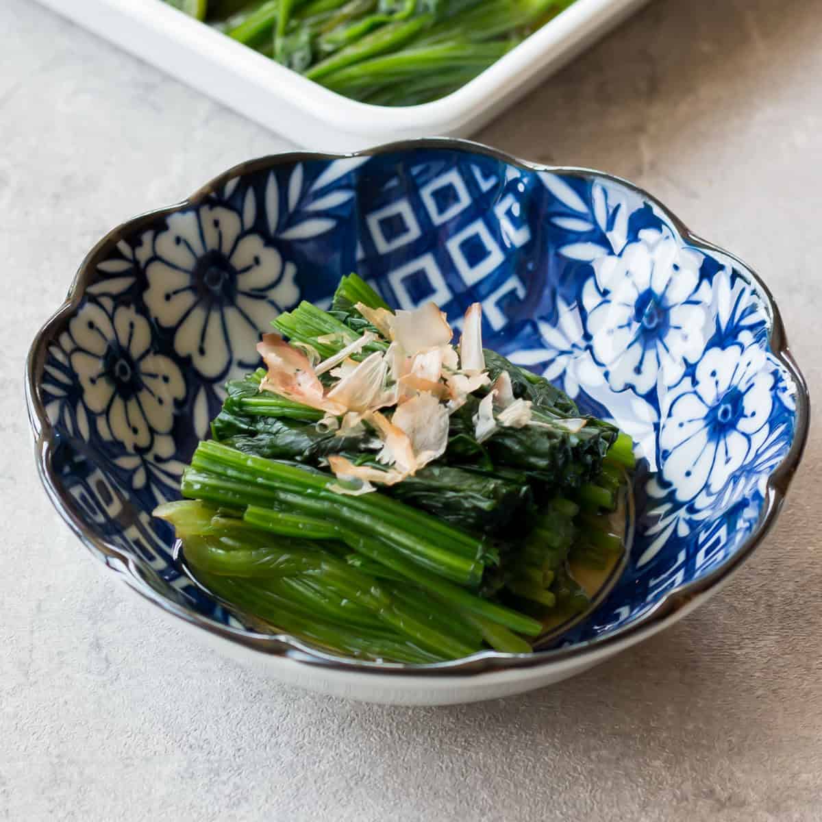 Spinach ohitashi served on a small plate with bonito flakes.